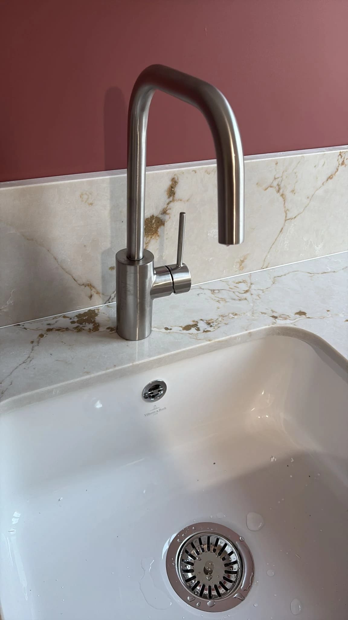 Évier en céramique blanche et robinet en inox devant une crédence en pierre veinée, appartement à Paris 16ᵉ