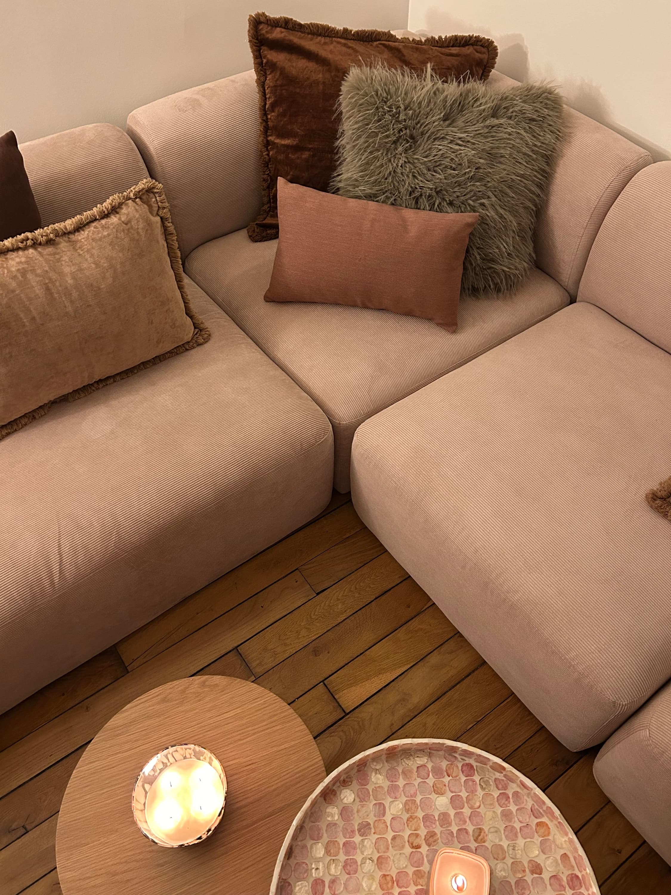 Canapé d'angle rose poudré, coussins en velours et fausse fourrure, tables basses sur parquet ancien, appartement à Paris 16ᵉ