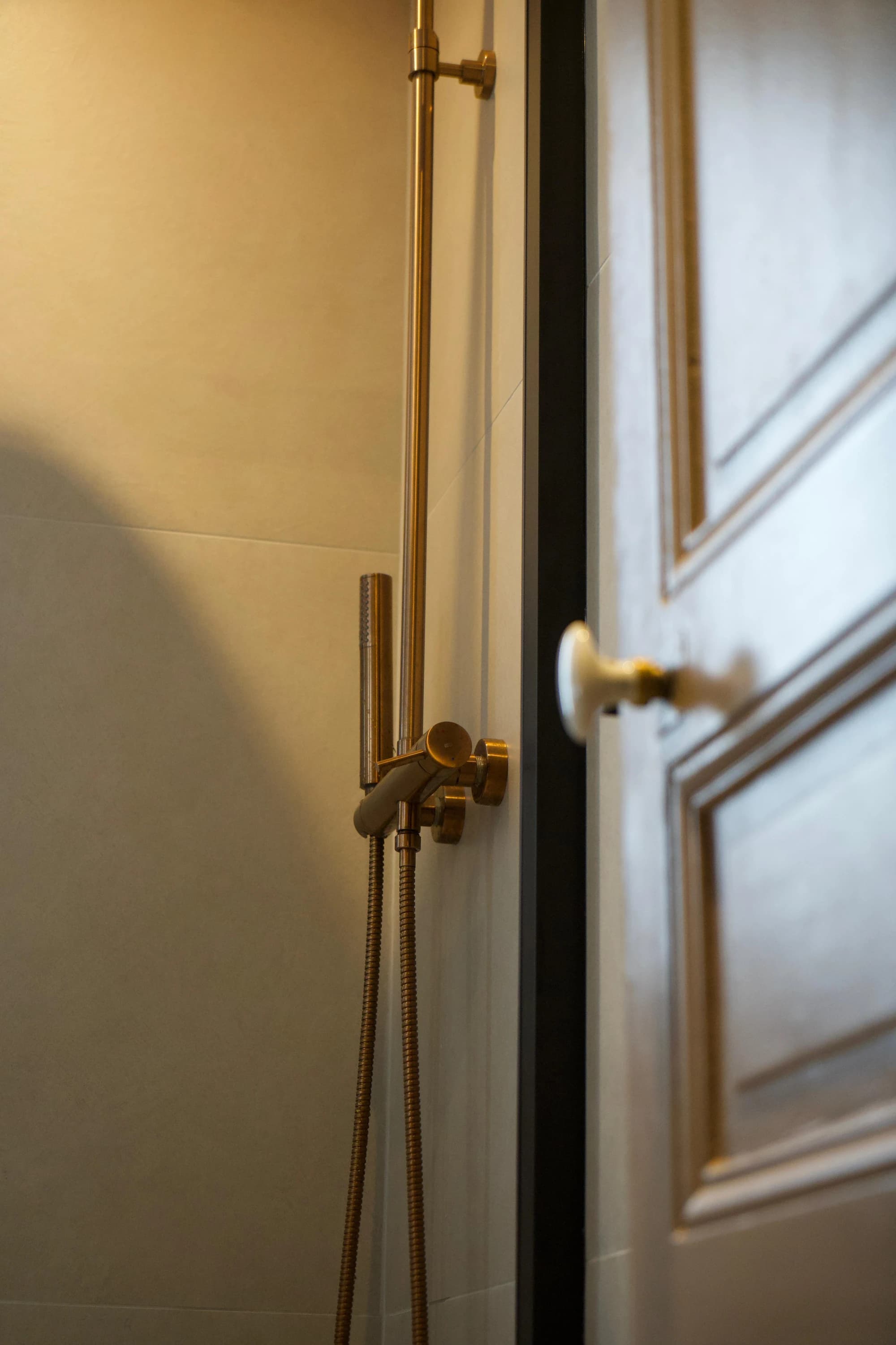 Détail d'une colonne de douche en laiton brossé contre une porte à moulures, salle de bains rue Ordener, Paris 18ᵉ